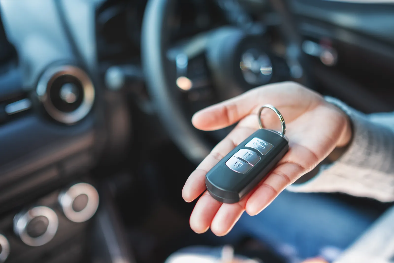 Hand hält einen Autoschlüssel im Innenraum eines Autos