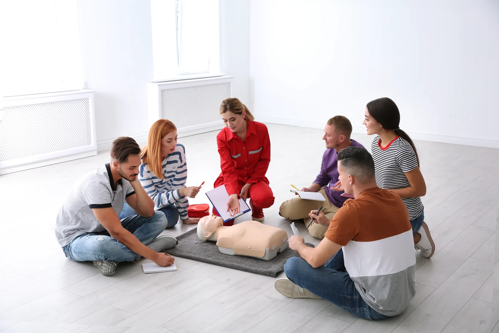 Gruppe übt mit einer Ausbilderin die Wiederbelebung an einer Übungspuppe