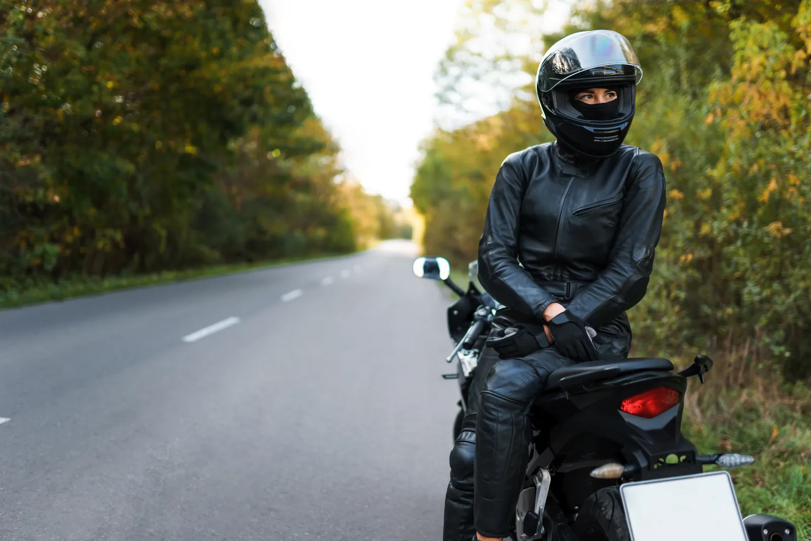 Motorradfahrerin mit Integralhelm und Lederkombi am Rand einer Landstraße