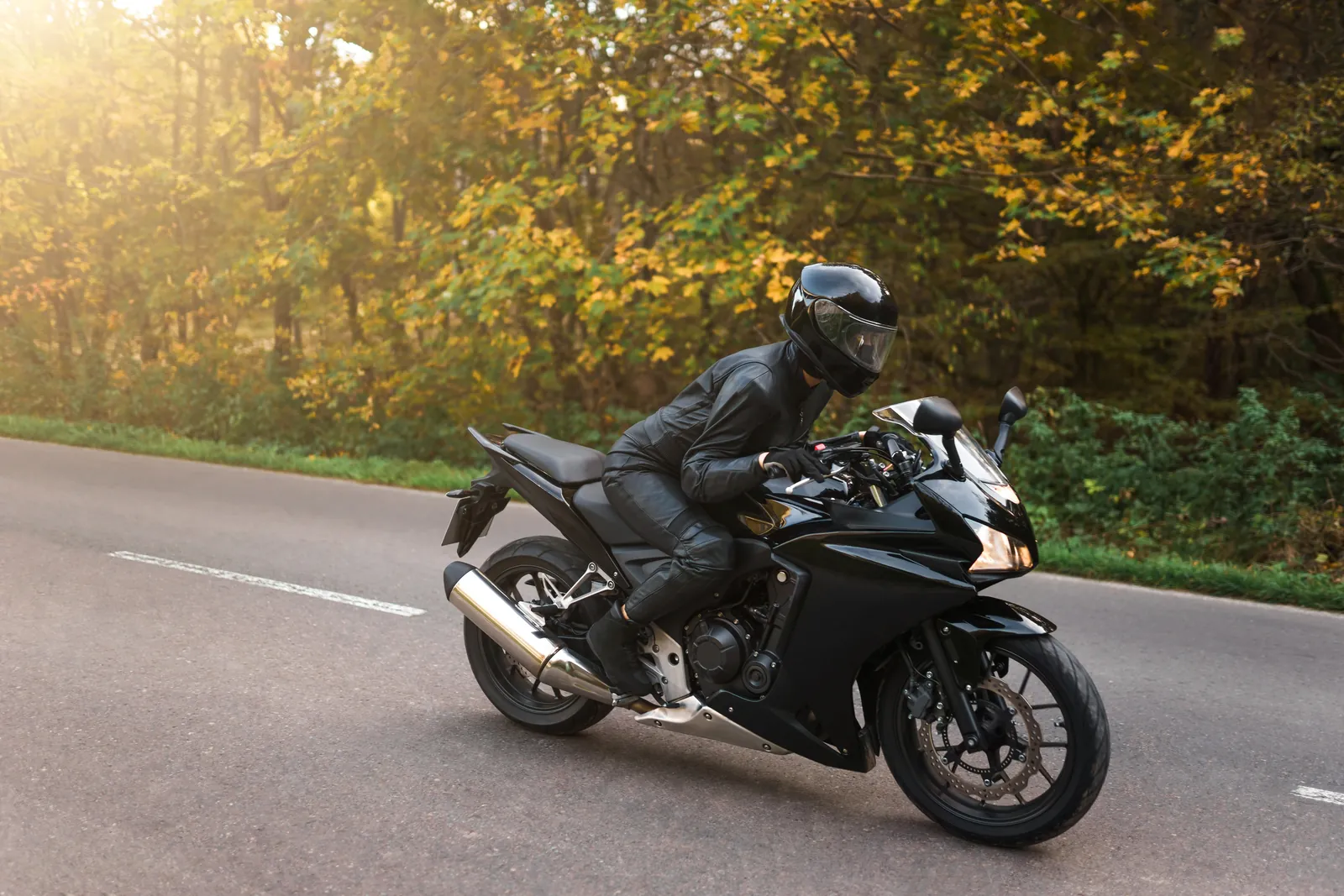 Motorradfahrer mit Integralhelm und Lederkombi auf einer Landstraße im Herbst