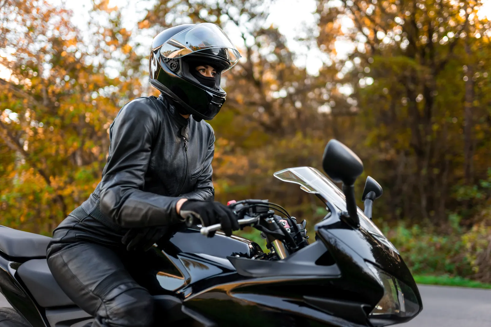 Motorradfahrerin mit Integralhelm und Lederkombi auf einem Sportmotorrad im Herbst